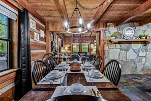 L’intérieur d’un chalet en bois comprend une table à manger pour quatre personnes, des murs en pierre et un lustre.