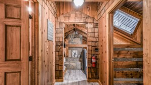 A wooden interior with a stone fireplace, a wooden staircase, and a skylight.