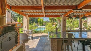 An outdoor patio with a grill, a glass table, and chairs.