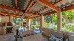 An outdoor kitchen area with a stone countertop, a grill, and a pergola structure.