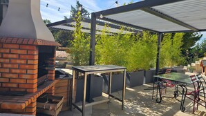 En udendørs patio med grill i mursten, et bord, stole og en pergola.
