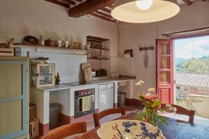 Una cocina rústica con una mesa de madera, un florero con flores y una puerta roja que da a un balcón.