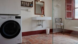 Un lavadero con lavadora, lavamanos y una silla.
