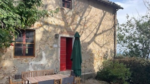 Un edificio de piedra rústico con puerta roja, una ventana y una mesa con sillas afuera.