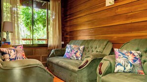 A cozy room with a green sofa set, floral cushions, a lamp, and a window with curtains. - Colibri Cabin (La Fortuna)