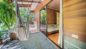 A modern interior with a sliding glass door leading to a garden, a hanging chair, and a bed with a view. - Colibri Cabin (La Fortuna)