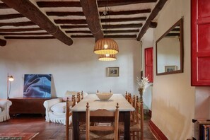A dining area with a wooden table, chairs, a hanging light fixture, and a red door.
