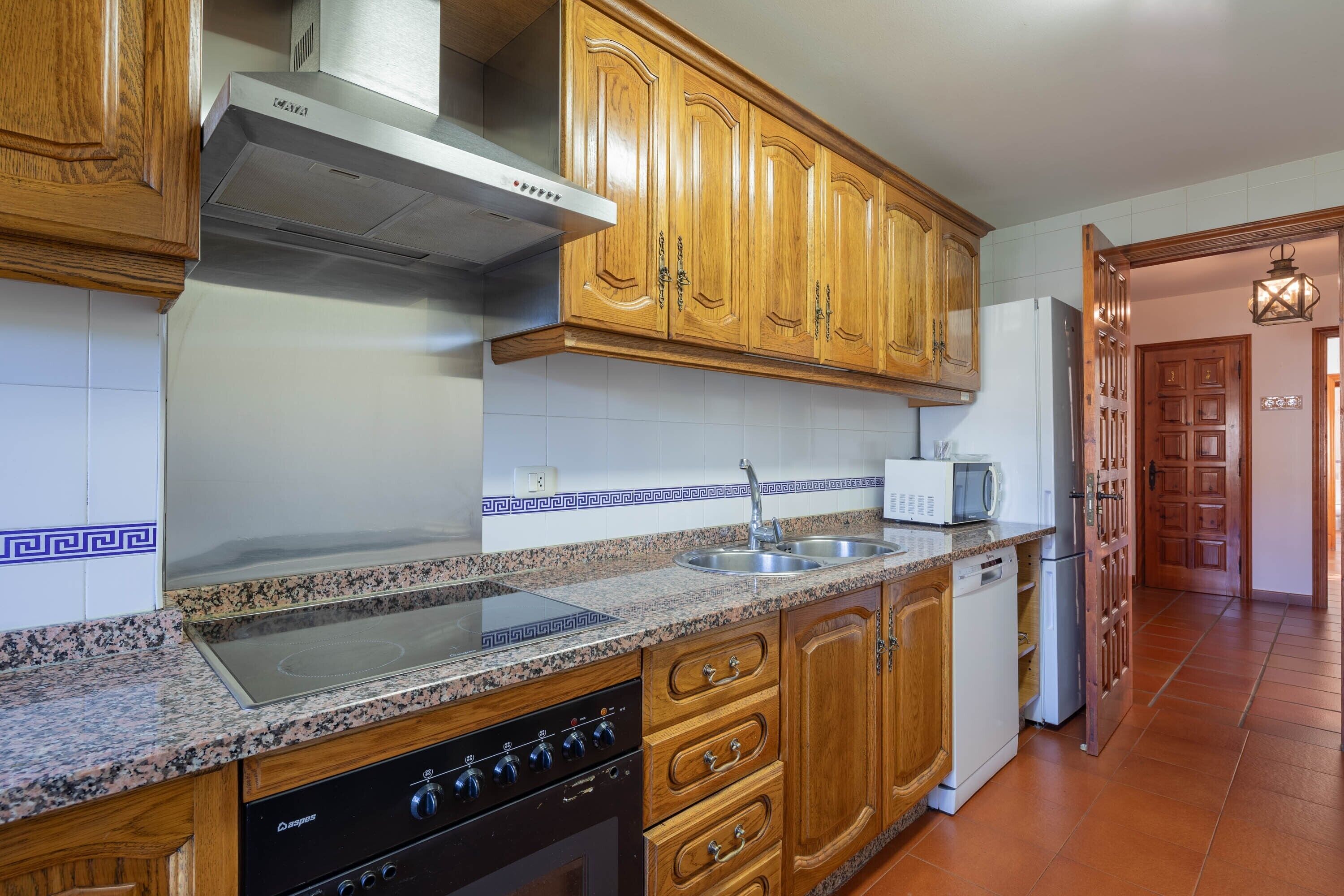 A kitchen with wooden cabinets, a stainless steel range hood, a microwave, and a dishwasher.
