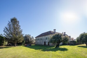 A stone house with a sloped roof, a small front yard, and a large tree to the left.