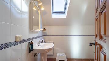 Un baño con tragaluz, azulejos blancos, un lavabo y un taburete pequeño.