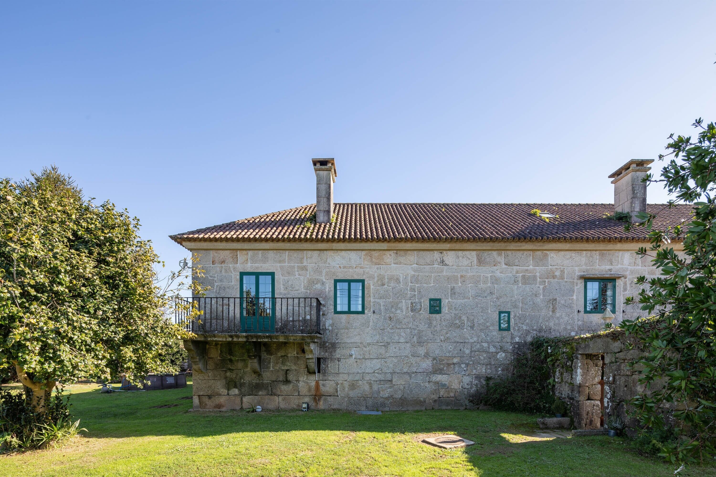 Un edificio de piedra con techo de tejas, balcón y un pequeño jardín.