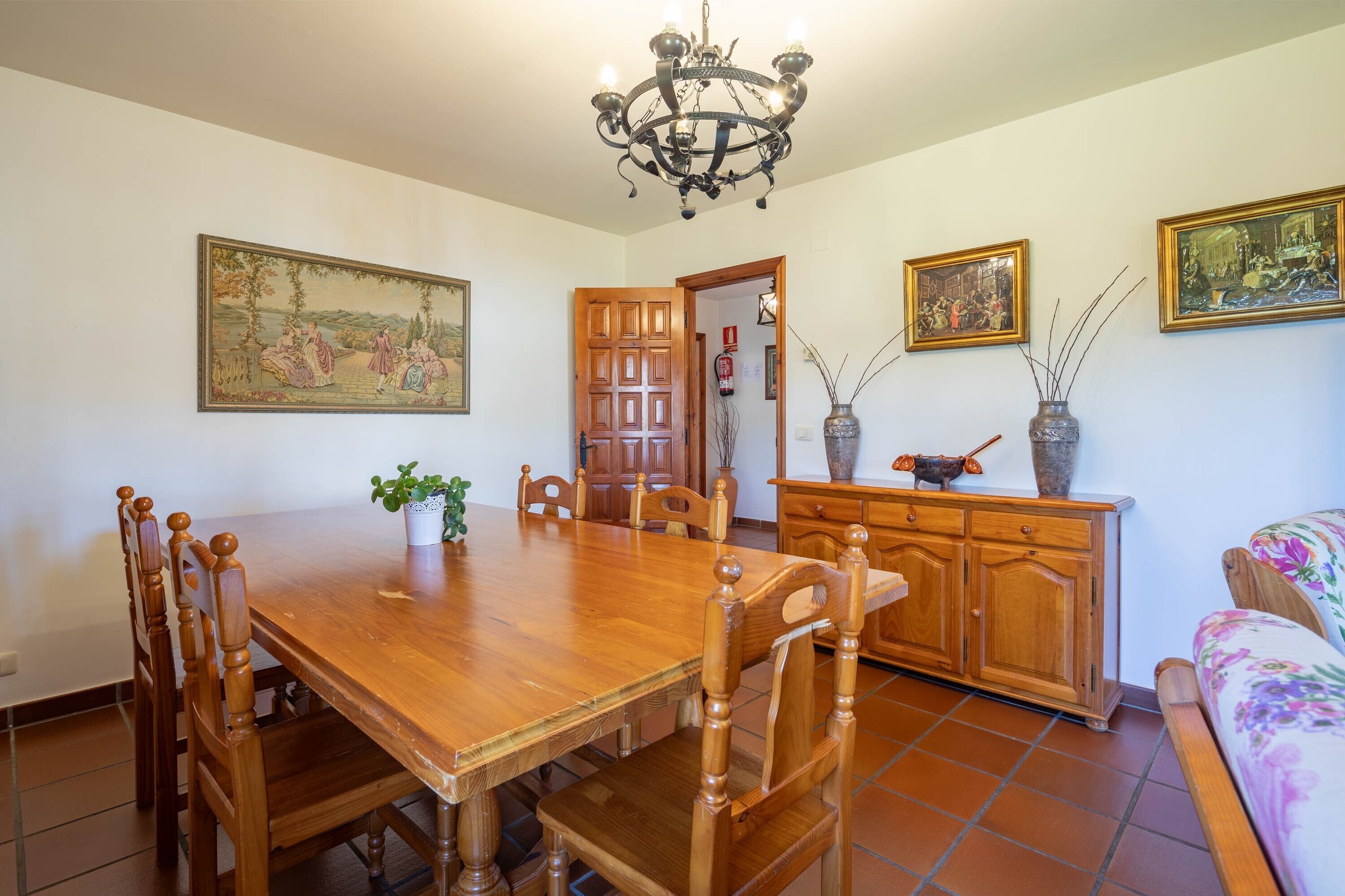 Zona pranzo con tavolo in legno, sedie, un lampadario e opere d'arte alle pareti.