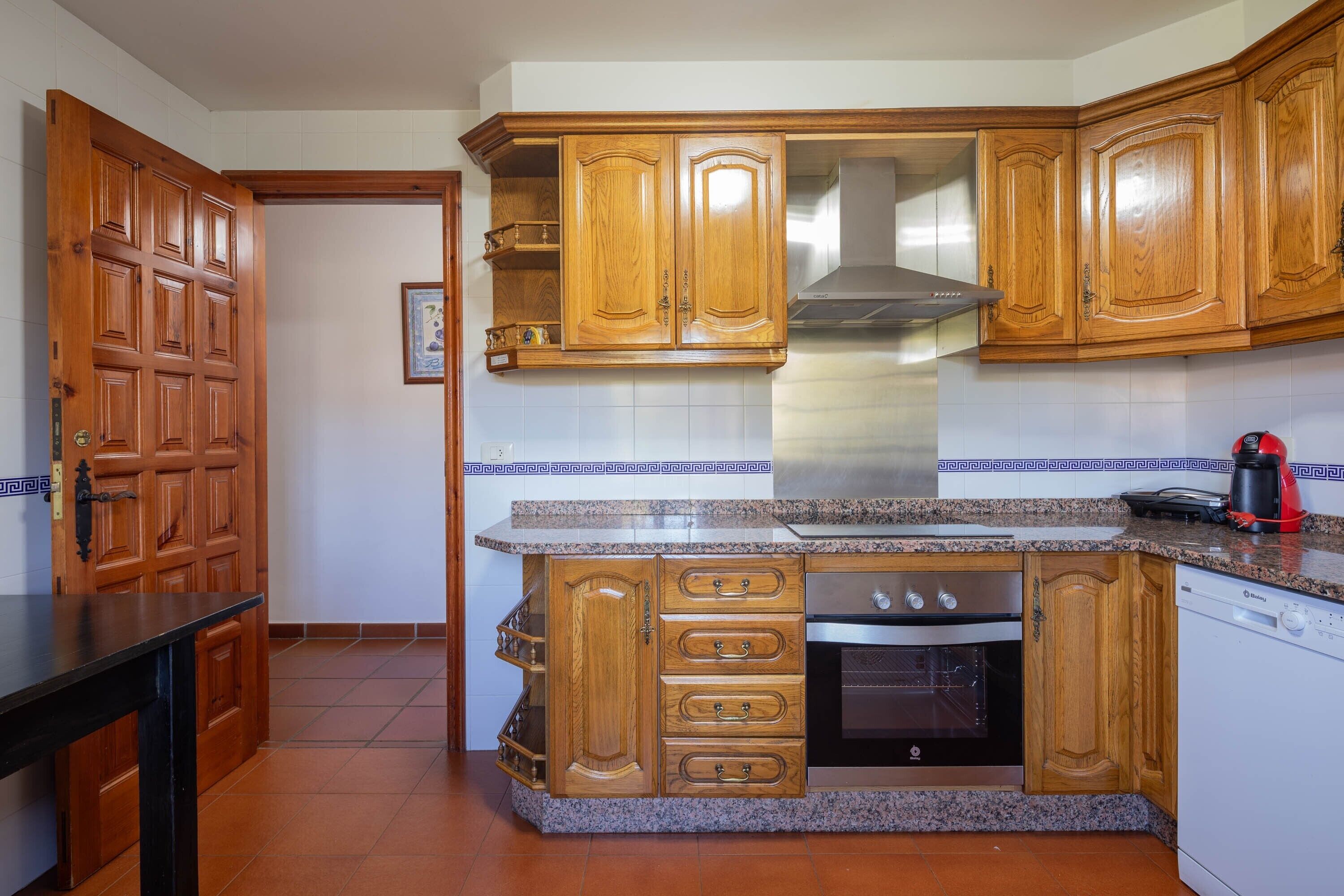 Una cocina con armarios de madera, encimera de granito, horno empotrado y lavavajillas.