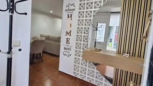 Une entrée d’hôtel moderne avec une pancarte « Bienvenue chez nous », un porte-manteau, un comptoir de réception et un sol carrelé.