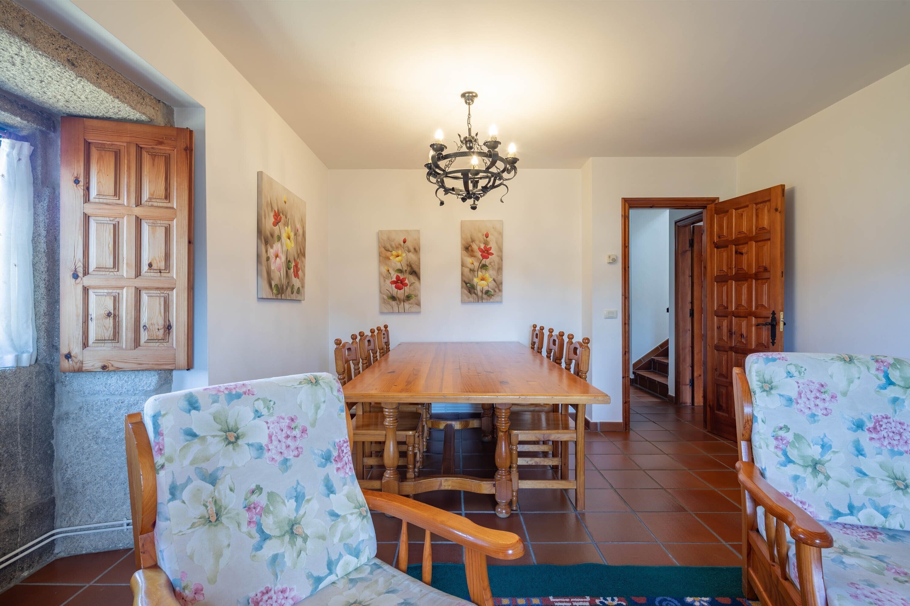 Comedor con mesa y sillas de madera, una araña y decoración floral en la pared.