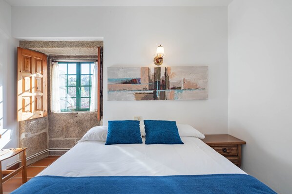 Una camera da letto con un letto, un comodino, una lampada a parete, una finestra con tende e un quadro.