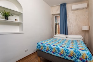 Ein Schlafzimmer mit einem Bett, einer Zimmerpflanze, einem Regal, einem Fenster und einer Klimaanlage.