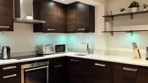 Una cocina moderna con armarios oscuros, horno empotrado, microondas y tostadora.