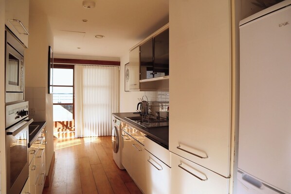 A kitchen with a microwave, oven, and dishwasher. There is a window with blinds, and a sink with a dish rack.