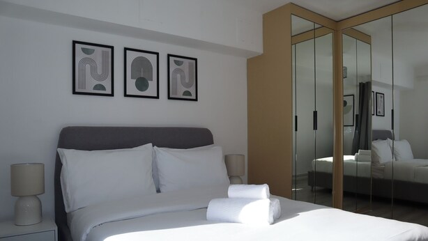 A modern hotel room with a large bed, a nightstand, a lamp, and three framed abstract artworks on the wall. - BnBNook - Soho and Regent’s Park - 1BR with Balcony (Greater London)
