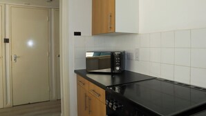 A kitchen with a microwave, stove, and wooden cabinets. - BnBNook - Soho and Regent’s Park - 1BR with Balcony (Greater London)