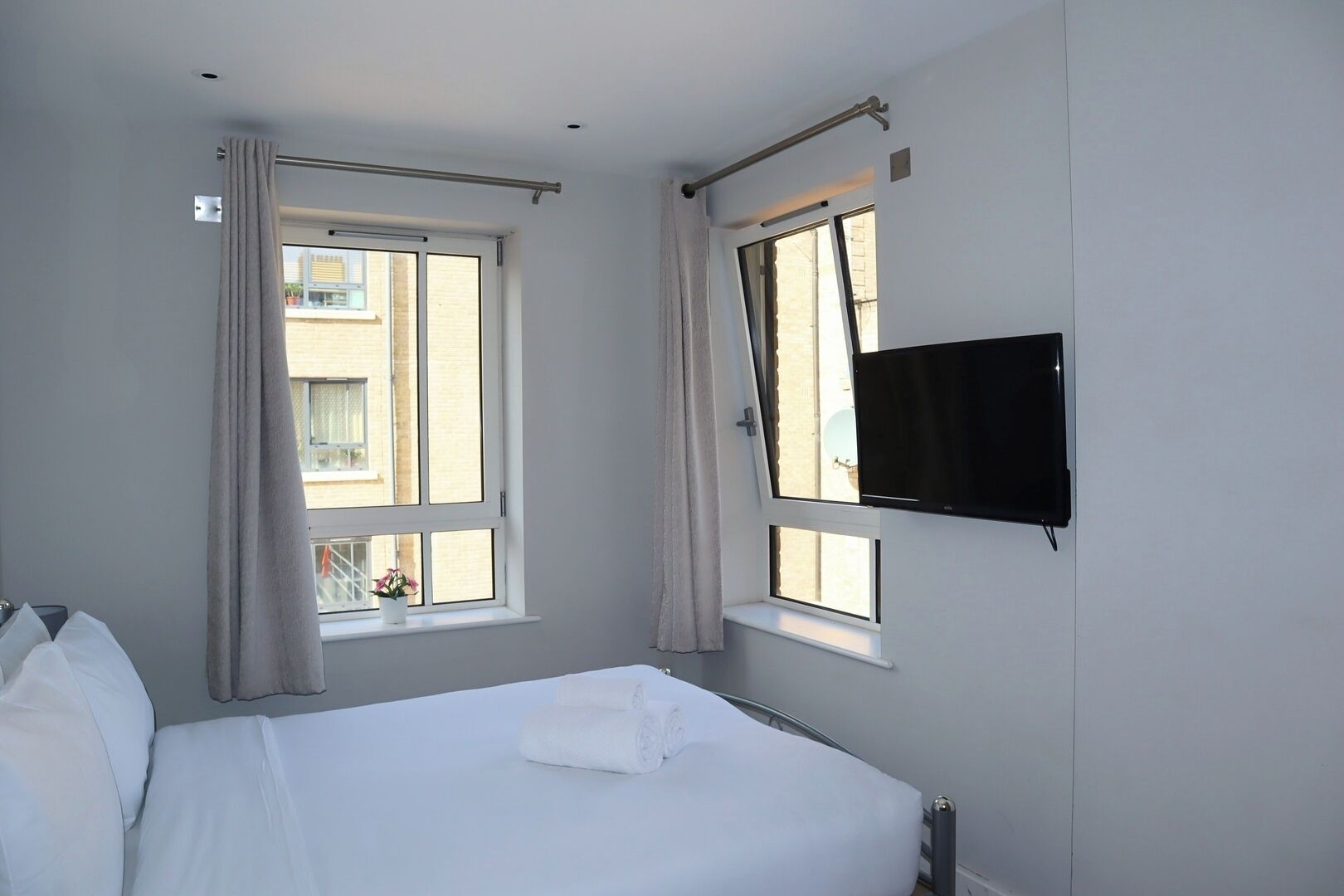 Une chambre d’hôtel avec un lit, deux fenêtres, un téléviseur fixé au mur et une tringle à rideaux.
