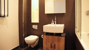 A modern bathroom with a white sink, dark tiled walls, a toilet, and a glass shower enclosure. - BnBNook - Camden 2BR with Terrace - King's Cross (Greater London)