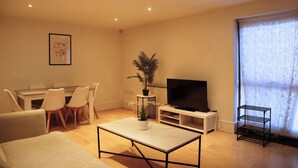 A living room with a TV, dining table, chairs, a coffee table, and a plant. - BnBNook - Camden 2BR with Terrace - King's Cross (Greater London)