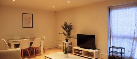 A living room with a TV, dining table, chairs, a coffee table, and a plant.