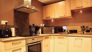 A modern kitchen with stainless steel appliances, wooden cabinets, and a built-in oven. - BnBNook - Camden 2BR with Terrace - King's Cross (Greater London)