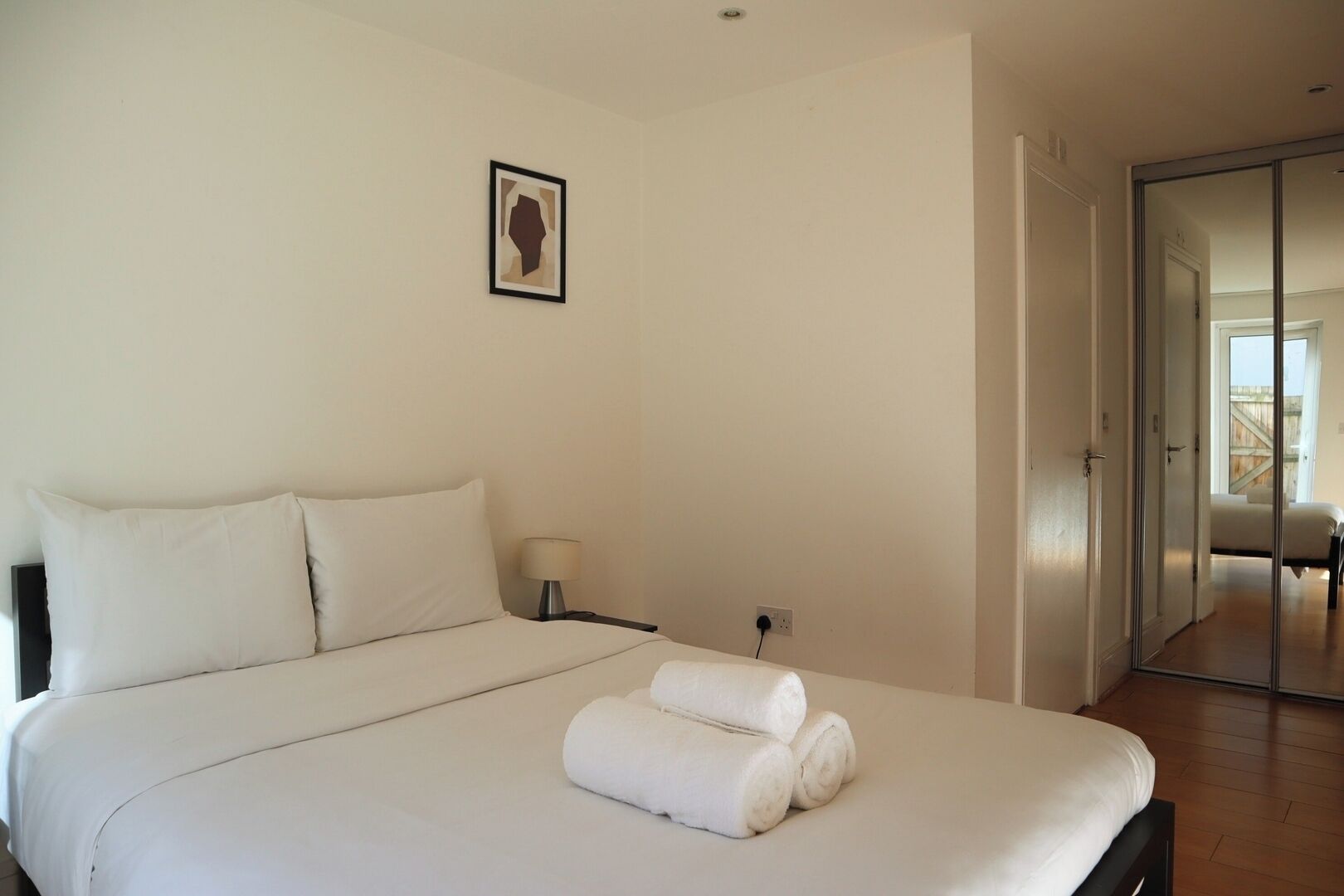 Un dormitorio con una cama, una mesita de noche, una lámpara y un cuadro en la pared.
