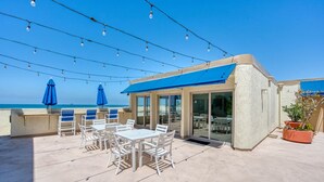 Um terraço no telhado com área de estar externa, luzes de festa e vista para a praia.