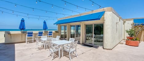 A rooftop patio with outdoor seating, string lights, and a view of the beach.