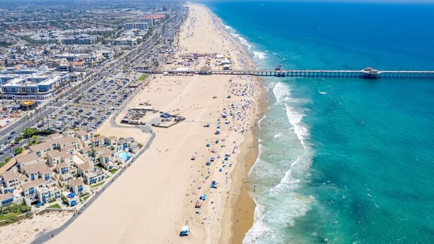 Paisagem costeira urbana com praia, um cais e uma área densamente construída com edifícios e carros estacionados.