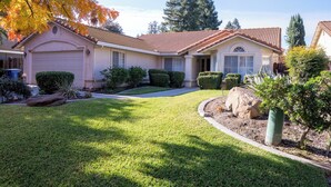 A single-story house with a garage, a well-maintained lawn, and a variety of shrubs and trees.