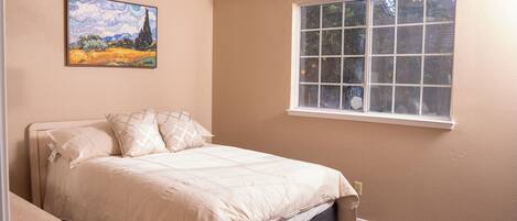 Un dormitorio con cama, ventana y un cuadro en la pared.