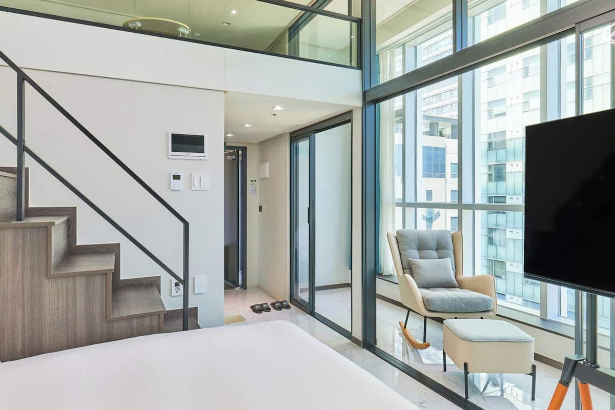 A modern interior with a staircase, a large window, a flat-screen TV, and a seating area.