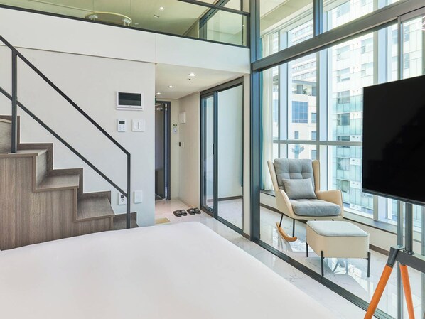 A modern interior with a staircase, a large window, a flat-screen TV, and a seating area. - NEWCZ CENTUM HOTEL (Busan)