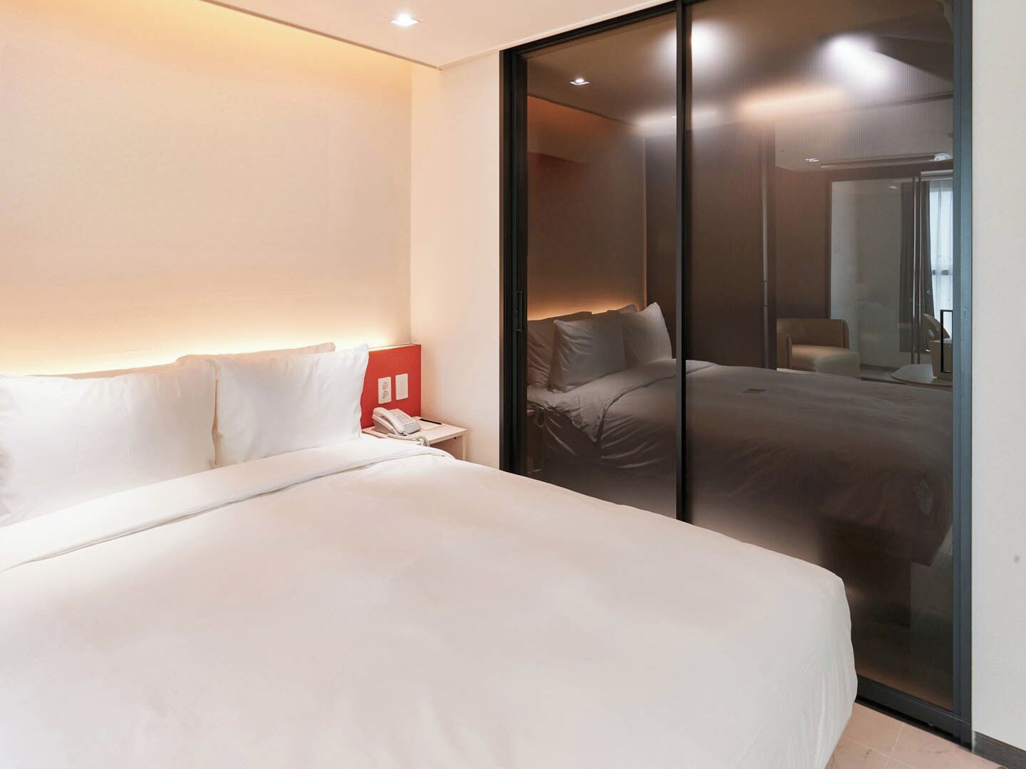 Una habitación de hotel moderna con una cama grande, un teléfono en la mesita de noche y una puerta corrediza de vidrio que da a un baño.