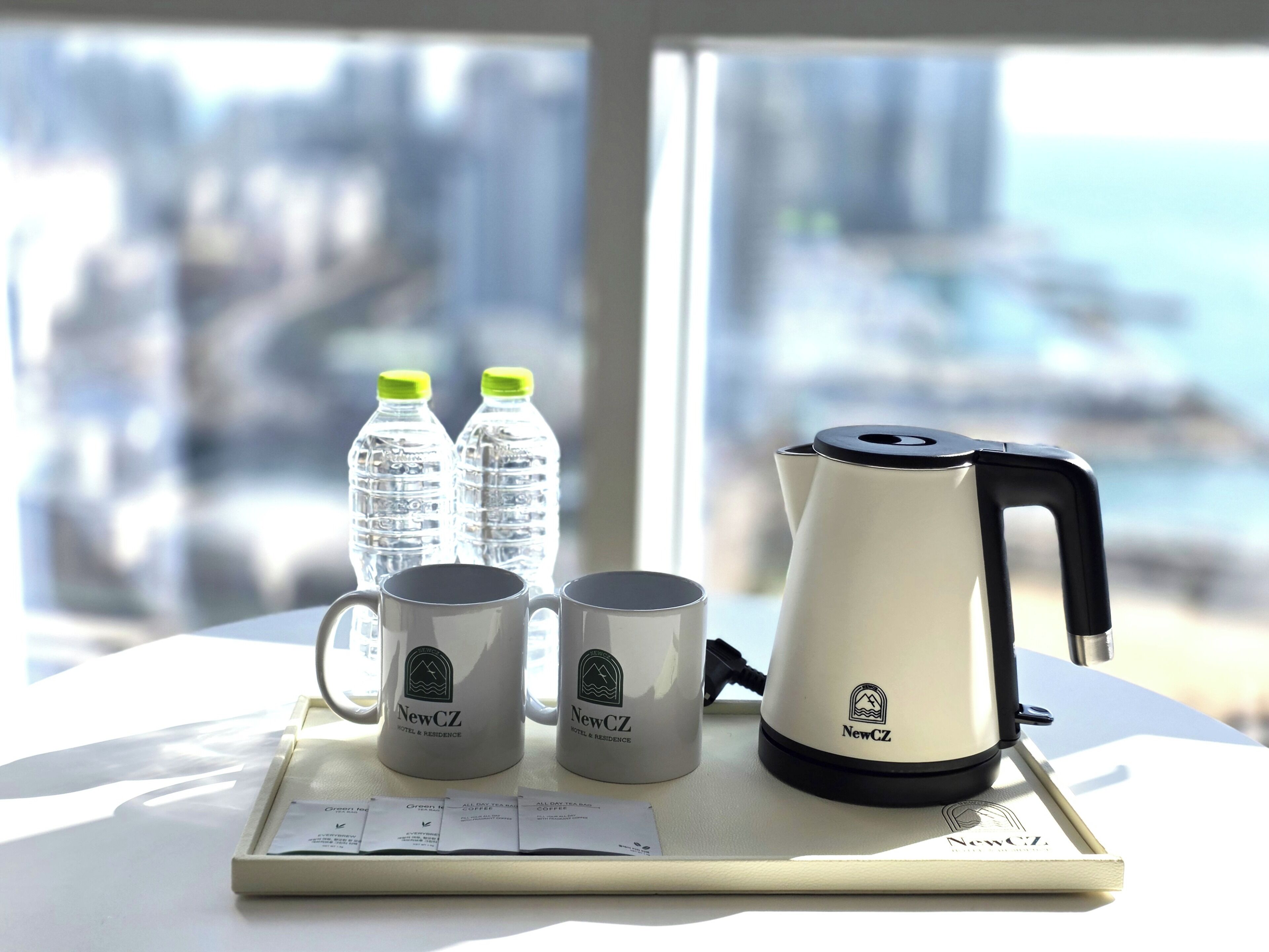 Uma mesa com cafeteira, duas chávenas e duas garrafas de água, sobre uma bandeja, com vista para a cidade ao fundo.