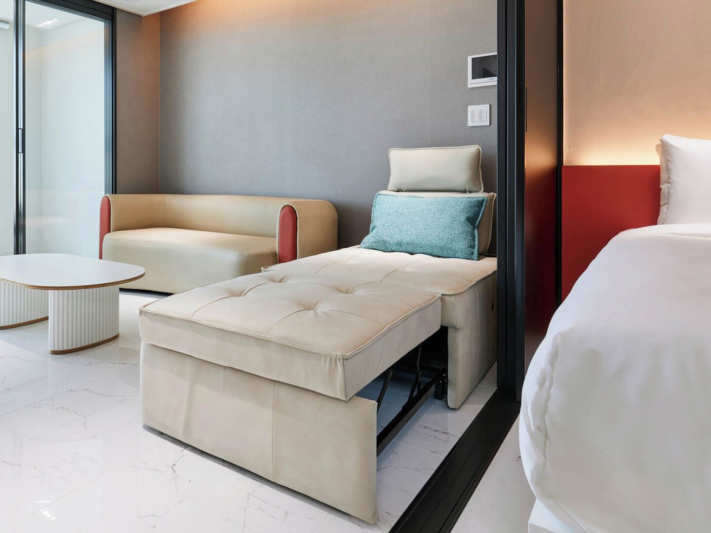 A modern hotel room with a sofa, a daybed, a small table, and a bed.