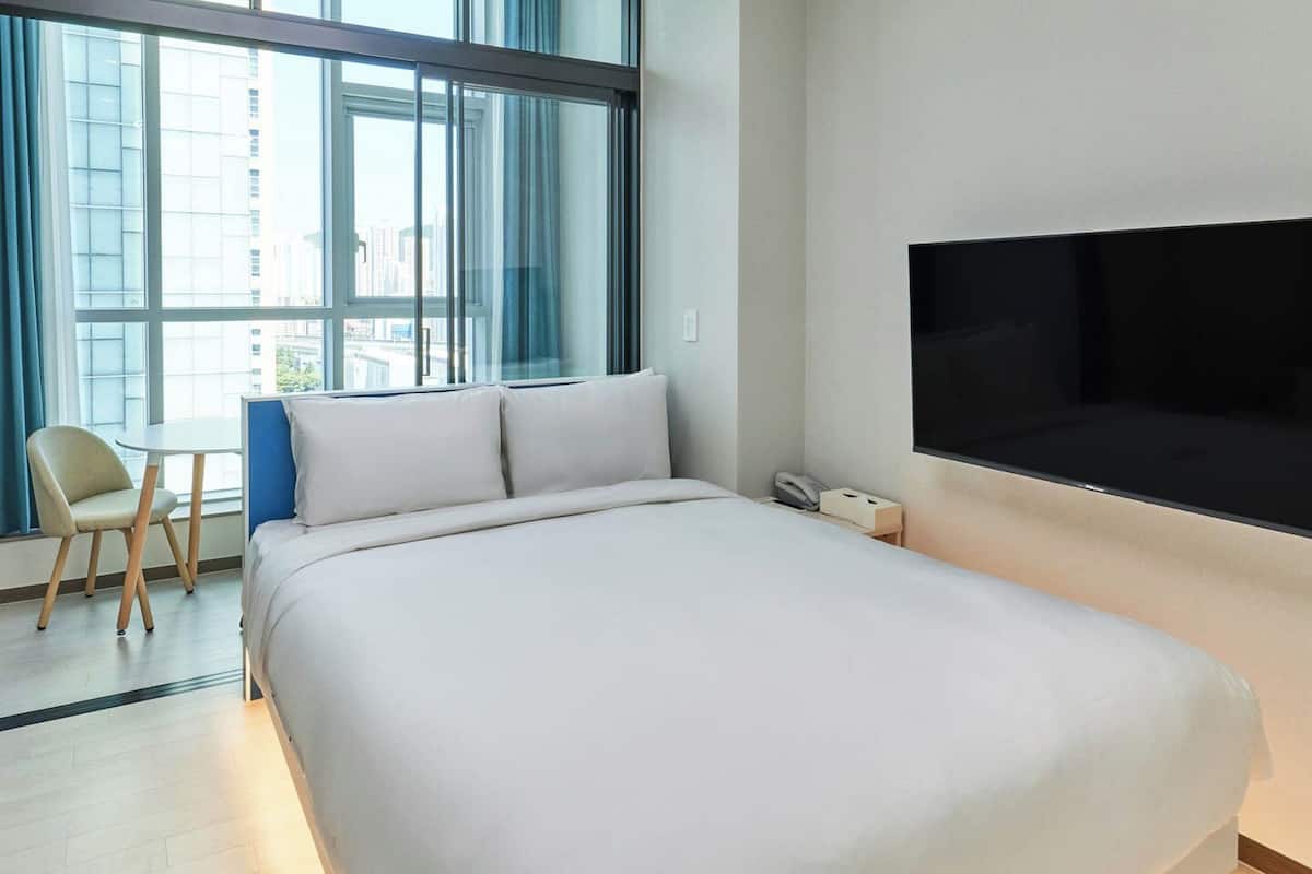 A modern hotel room with a large bed, a desk, and a TV mounted on the wall.