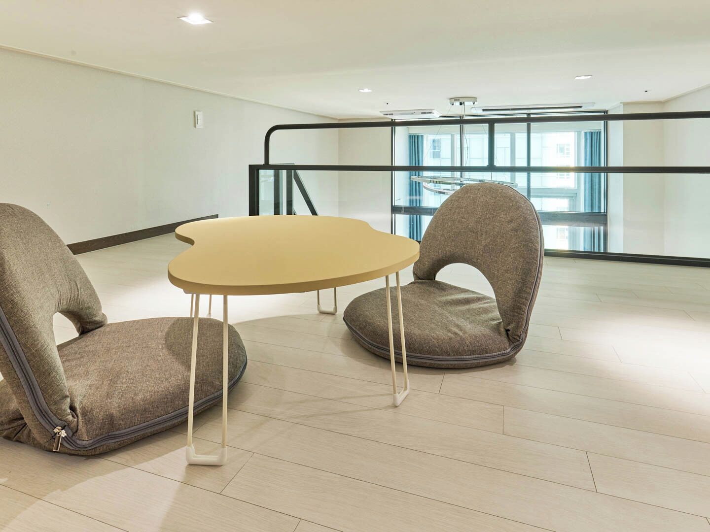 Quarto moderno com mesa redonda e duas cadeiras, grandes janelas e guarda-corpo de vidro.