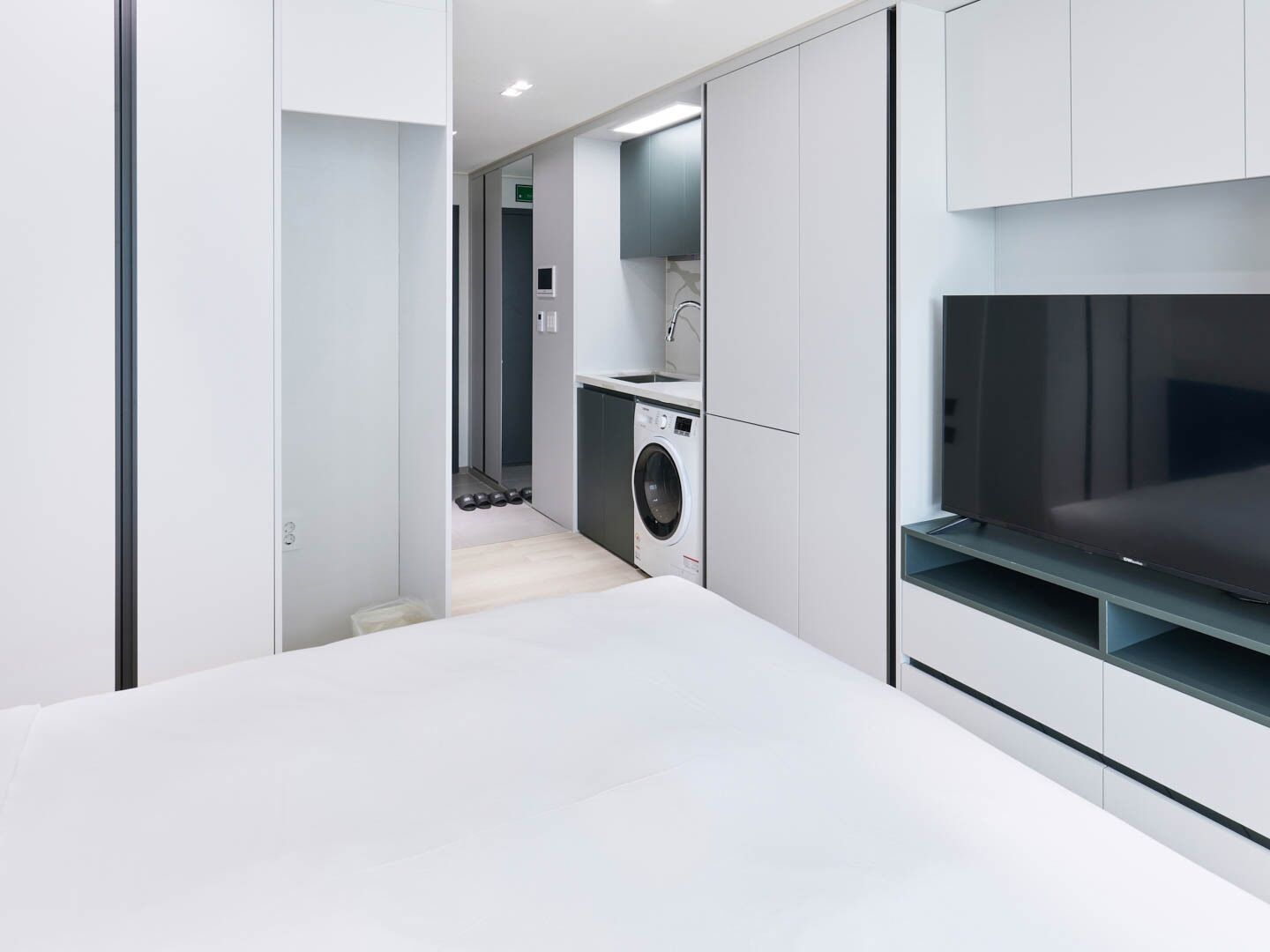 A modern, minimalist bathroom with a large mirror, a built-in washing machine, and a sleek vanity with a TV.