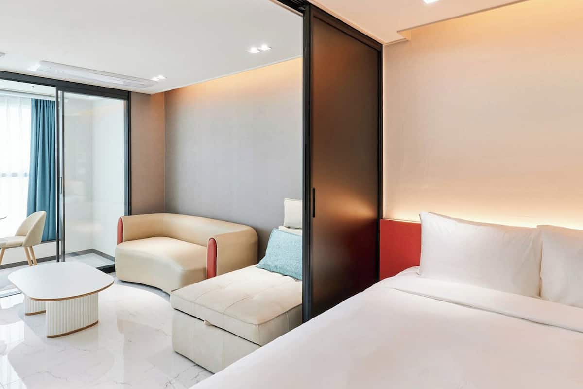 A modern hotel room with a large bed, a sofa, a small table, and a chair.