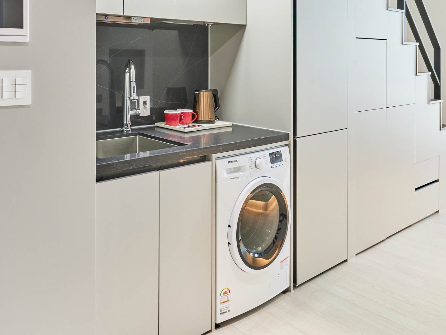 Una cocina moderna con lavadora integrada, cafetera y fregadero.