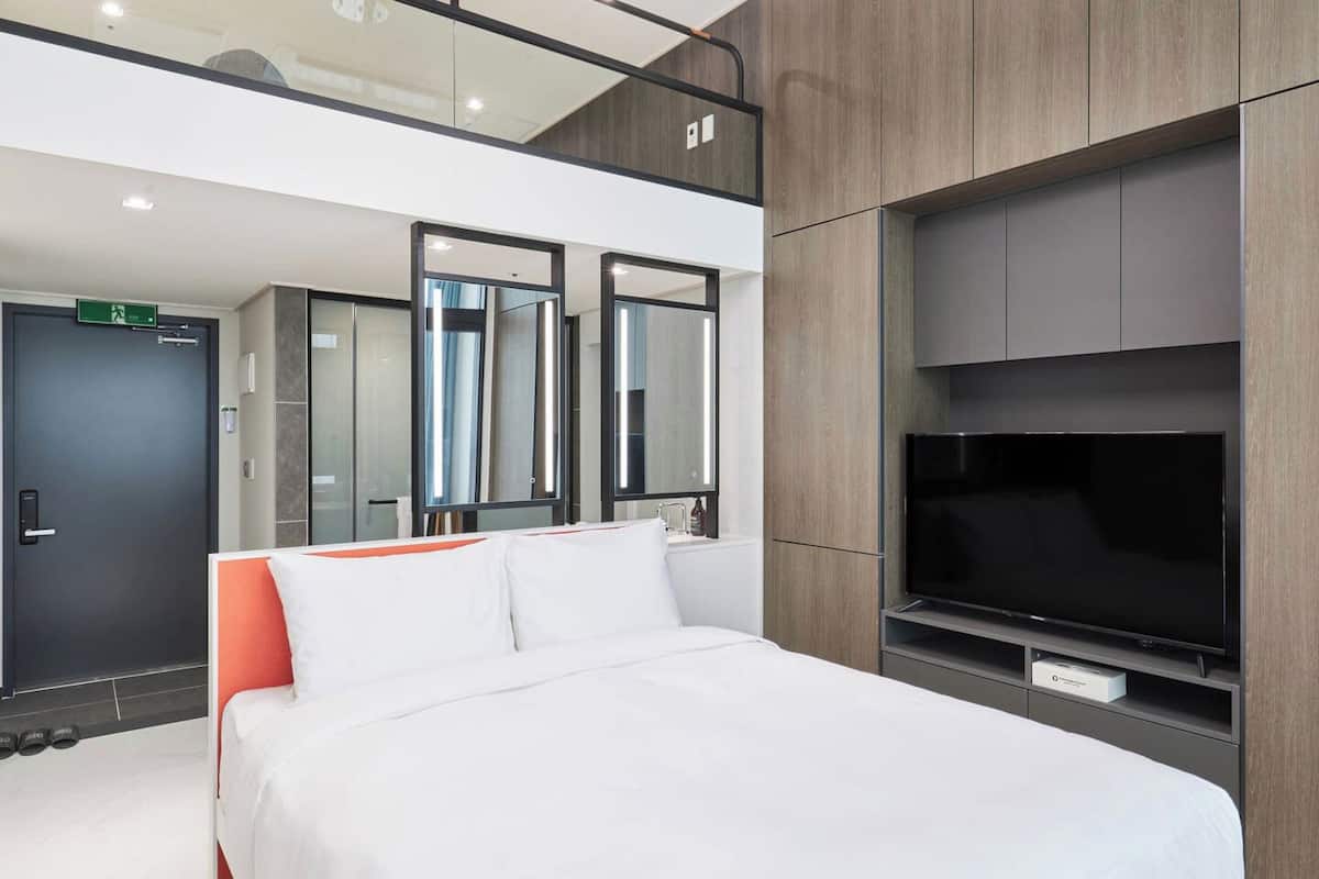 A modern hotel room with a large bed, a flat-screen TV, and a mirror above the bed.