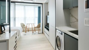 A modern kitchen with a built-in washer, a dining area with chairs, and a large window with curtains. - NEWCZ CENTUM HOTEL (Busan)