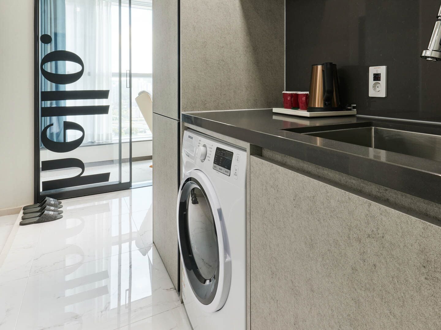 A modern kitchen with a built-in washing machine, a countertop, and a window with a view.