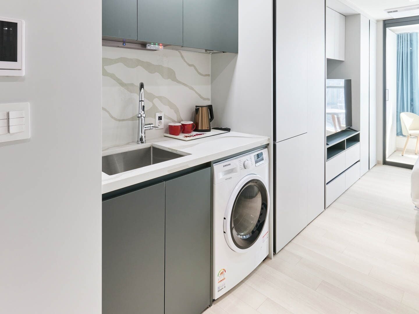 A modern kitchen with a built-in washing machine, a sink, and a coffee maker.